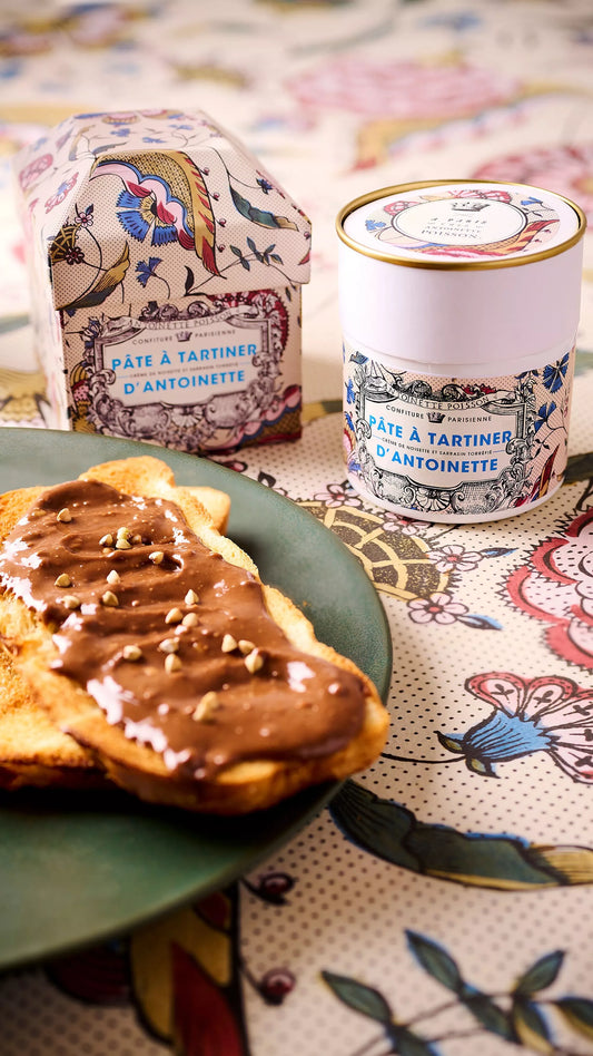 Bread with chocolate spread on a plate next to a jar of chocolate spread on a decorative tablecloth.