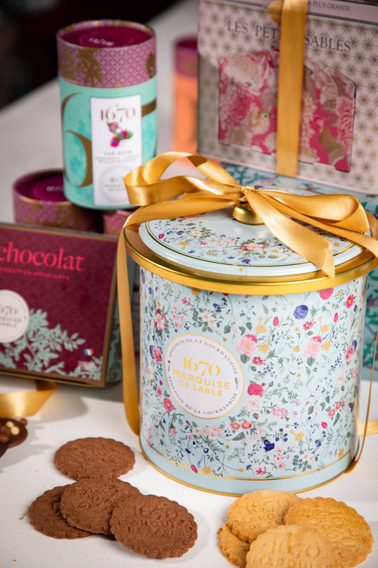Decorative cookie tin with cookies on a table, surrounded by other gift items.