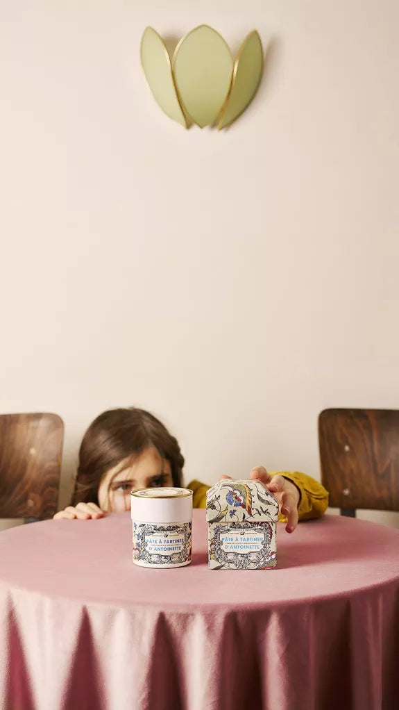 Child at a table with two decorative jars, one pink and one white, against a light pink wall.