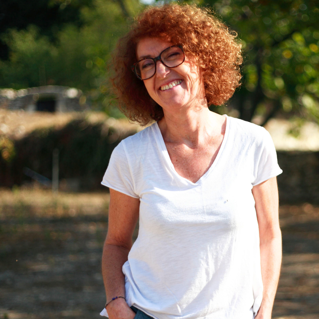 Woman with curly hair and glasses wearing a white t-shirt outdoors.
