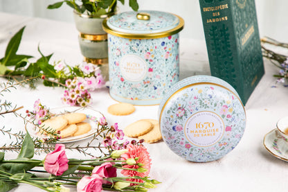 Decorative tea canisters with floral designs on a table with cookies and flowers.