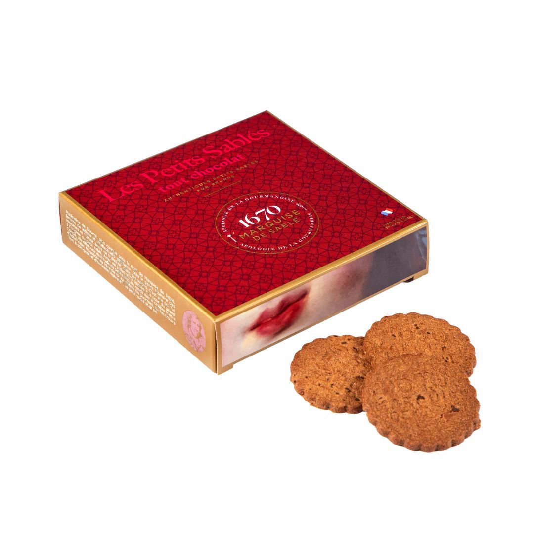 Red box of Les Petits Sablés cookies with two cookies in front on a white background